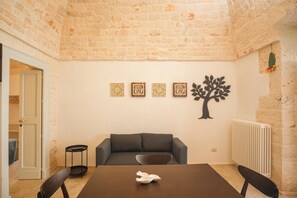 A room with a stone wall, a sofa, a table, and wall art including a tree and patterned designs. - Stone House—A Stone House in the Heart of Alberobello (Alberobello)