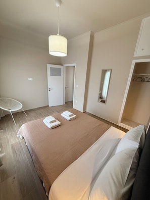 Habitació d'hotel amb un llit gran, una cadira, un armari i una porta que condueix a una altra habitació.