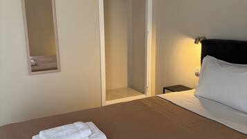Una camera d'albergo con un letto, due asciugamani piegati con cura, un comodino con una lampada e un armadio con uno specchio.