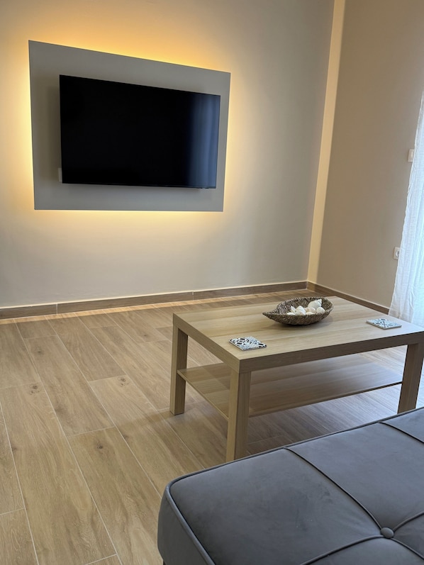 Un saló modern amb televisió de pantalla plana penjada a la paret, una taula de centre de fusta amb objectes decoratius i un sofà gris.