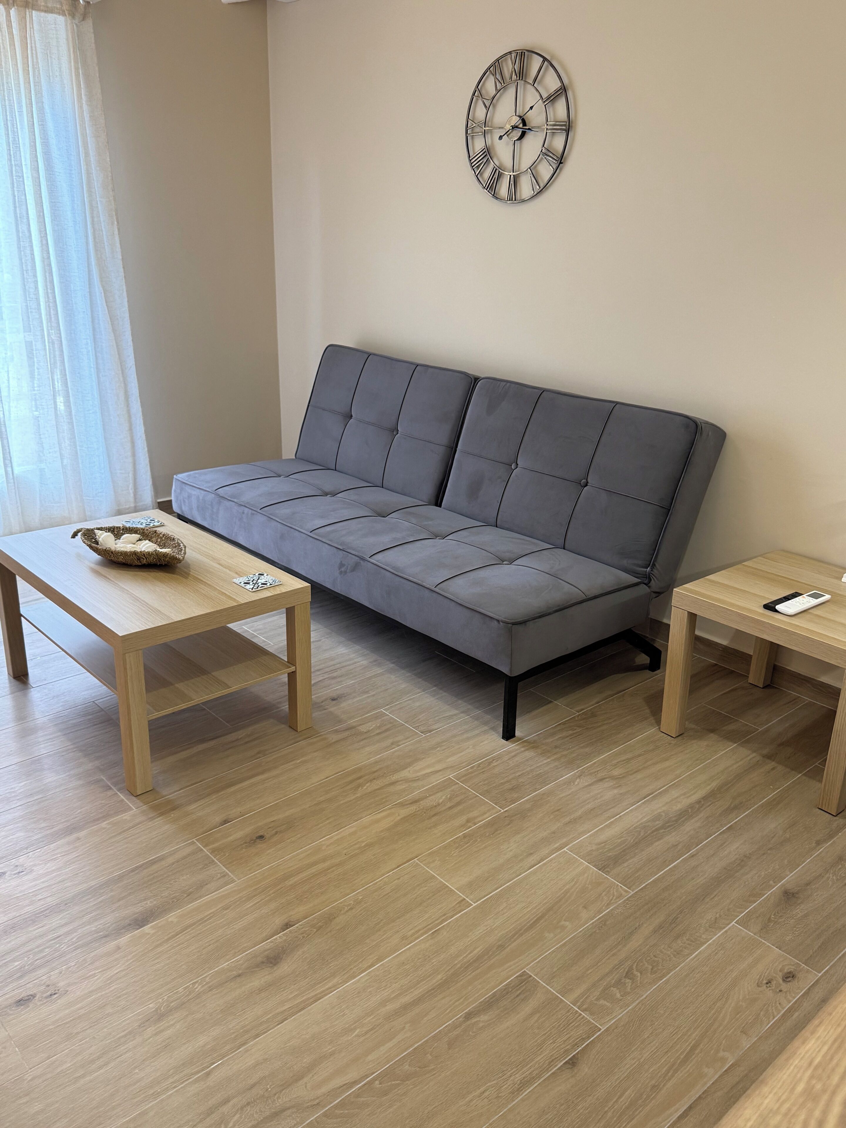 Un soggiorno moderno con un divano grigio, due tavolini in legno e una sveglia a parete.