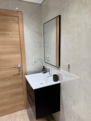 Un bany modern amb una porta de fusta, un lavabo blanc, un armari negre i un mirall amb marc negre.