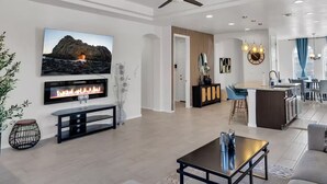 A modern living room with a fireplace, a flat-screen TV, and a dining area with a kitchen in the background. - Modern Rio Rancho - Fireplace, Private Yard (Rio Rancho)