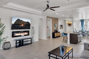 A modern living room with a fireplace, a flat-screen TV, and a dining area with a kitchen in the background. - Modern Rio Rancho - Fireplace, Private Yard (Rio Rancho)