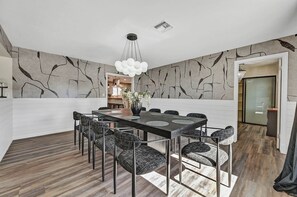 A modern dining room with a rectangular table, black upholstered chairs, a vase with white flowers, and a unique wall design. - 5,000 sqft Vegas Getaway w Private Pool Near Strip (Las Vegas)