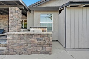A stone-built outdoor kitchen area with a built-in grill, a window, and a covered patio space. - 5,000 sqft Vegas Getaway w Private Pool Near Strip (Las Vegas)