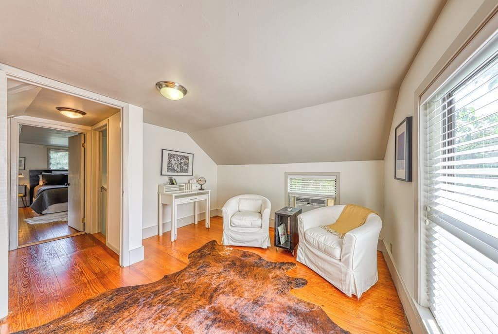 A room with a wooden floor, a white leather sofa, a white armchair, a small table, and a large rug.