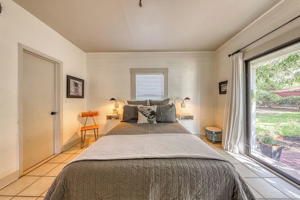 A bedroom with a large bed, bedside tables, a window with blinds, and a door.