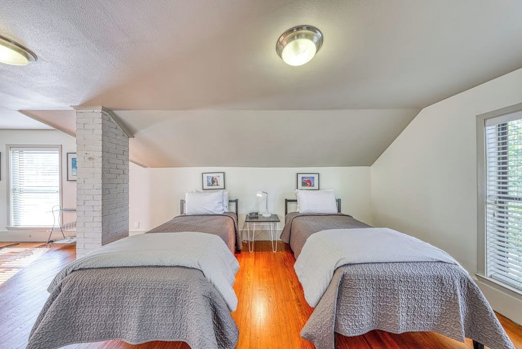 A room with two beds, a brick wall, a small table, and a window.
