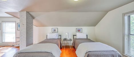A room with two beds, a brick wall, a small table, and a window.
