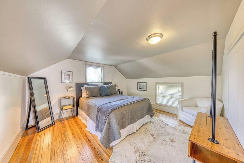 A bedroom with a bed, bedside tables, a mirror, a white sofa, and a wooden bench.