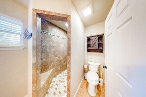 Ein Badezimmer mit Dusche, Toilette und einem kleinen Fenster.