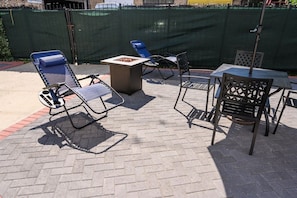 An outdoor patio area with a fire pit, metal chairs, and a table. - Fun Gaming Apartment w/Free Parking (Chicago)