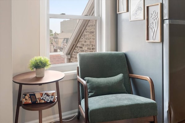 A corner room with a green upholstered chair, a small round table with a potted plant, and a framed picture on the wall.