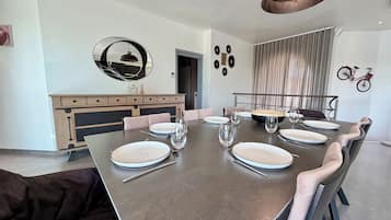 Een eetruimte met een grote tafel voor zes personen, een moderne hanglamp en een fiets aan de muur.