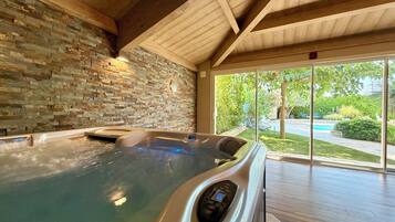 Een wellnessruimte met een stenen muur, een jacuzzi en uitzicht op de natuur.