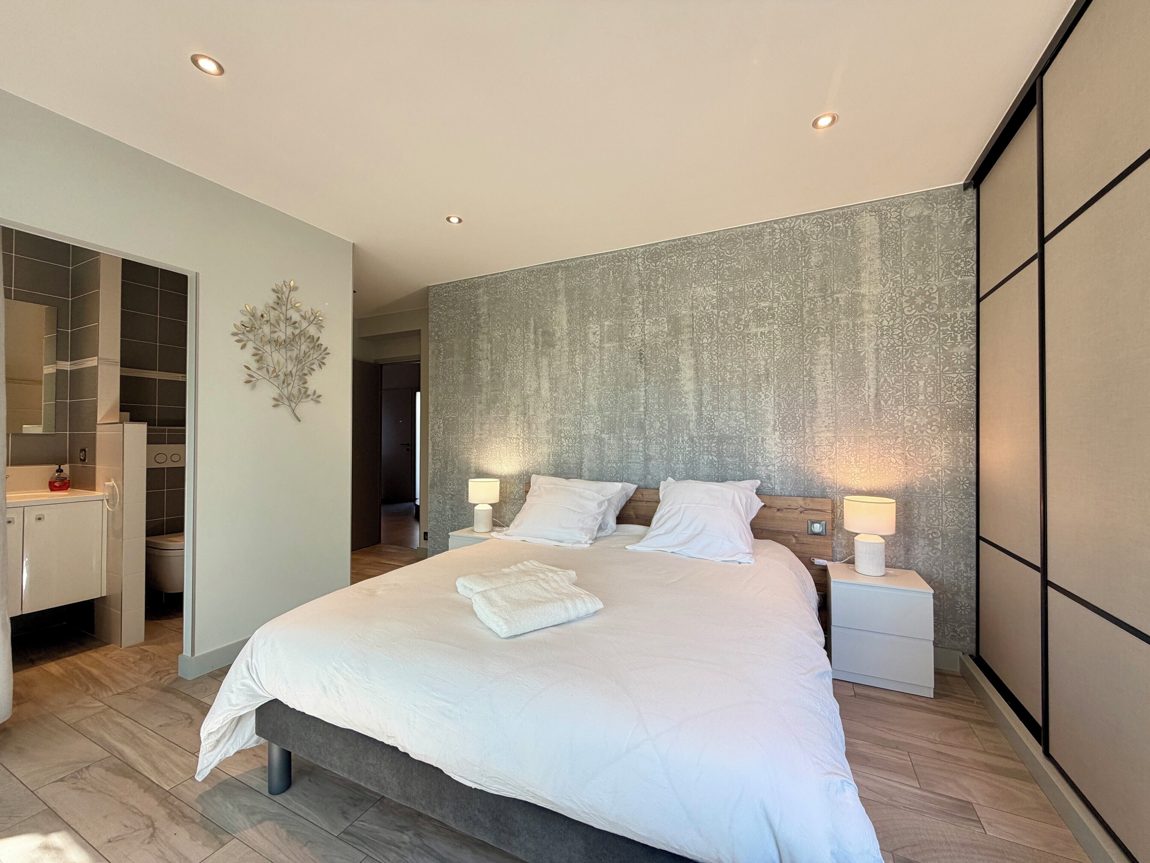 Een moderne slaapkamer met een groot bed, nachtlampjes en een inloopkast.