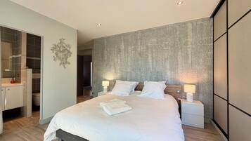 Een moderne slaapkamer met een groot bed, nachtlampjes en een inloopkast.