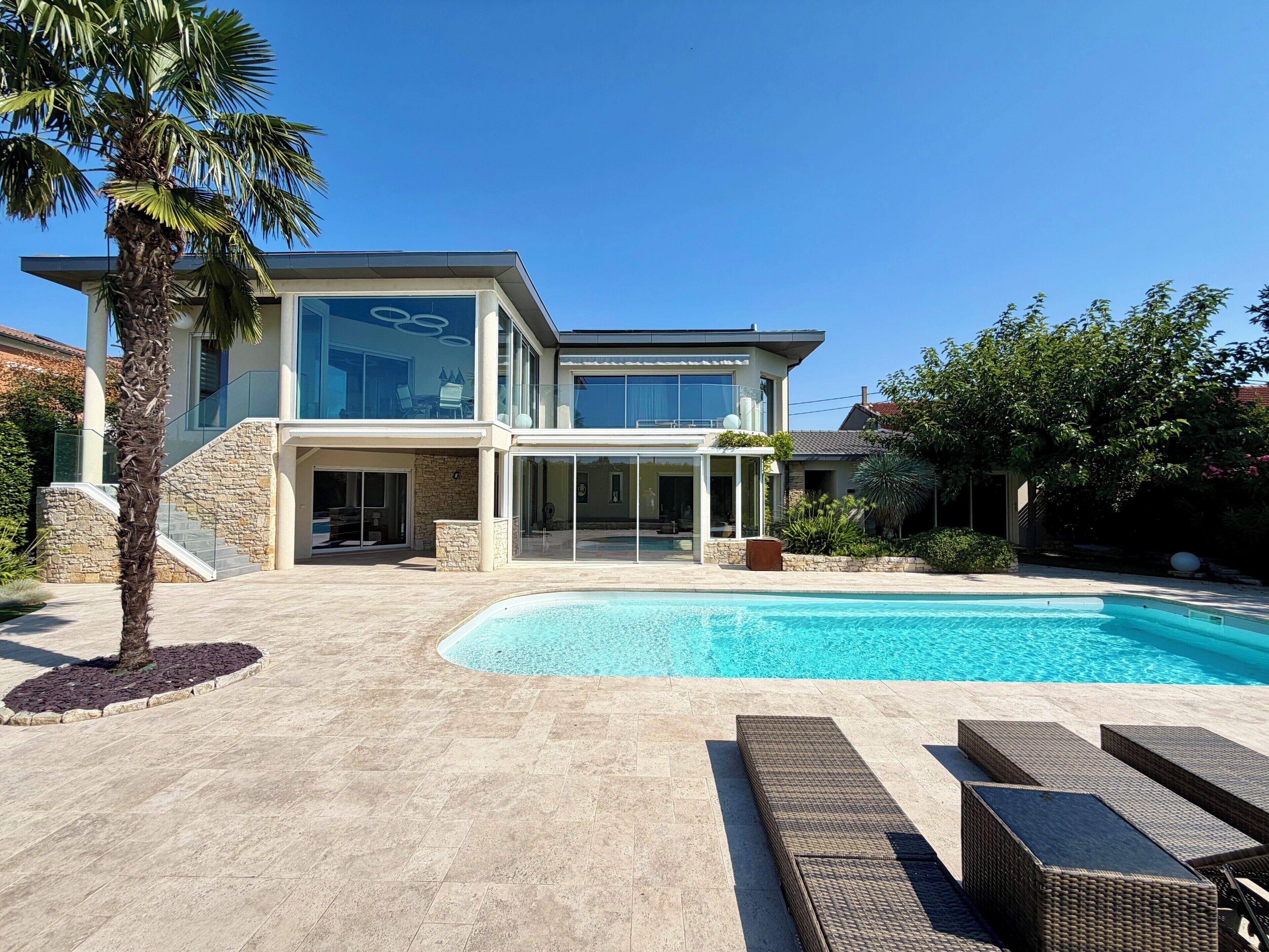 Une maison moderne à deux étages, dotée d’une piscine, de mobilier d’extérieur et d’un escalier en pierre.