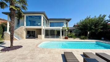 Une maison moderne à deux étages, dotée d’une piscine, de mobilier d’extérieur et d’un escalier en pierre.