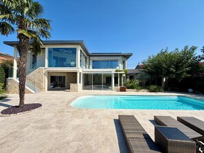 Une maison moderne à deux étages, dotée d’une piscine, de mobilier d’extérieur et d’un escalier en pierre.