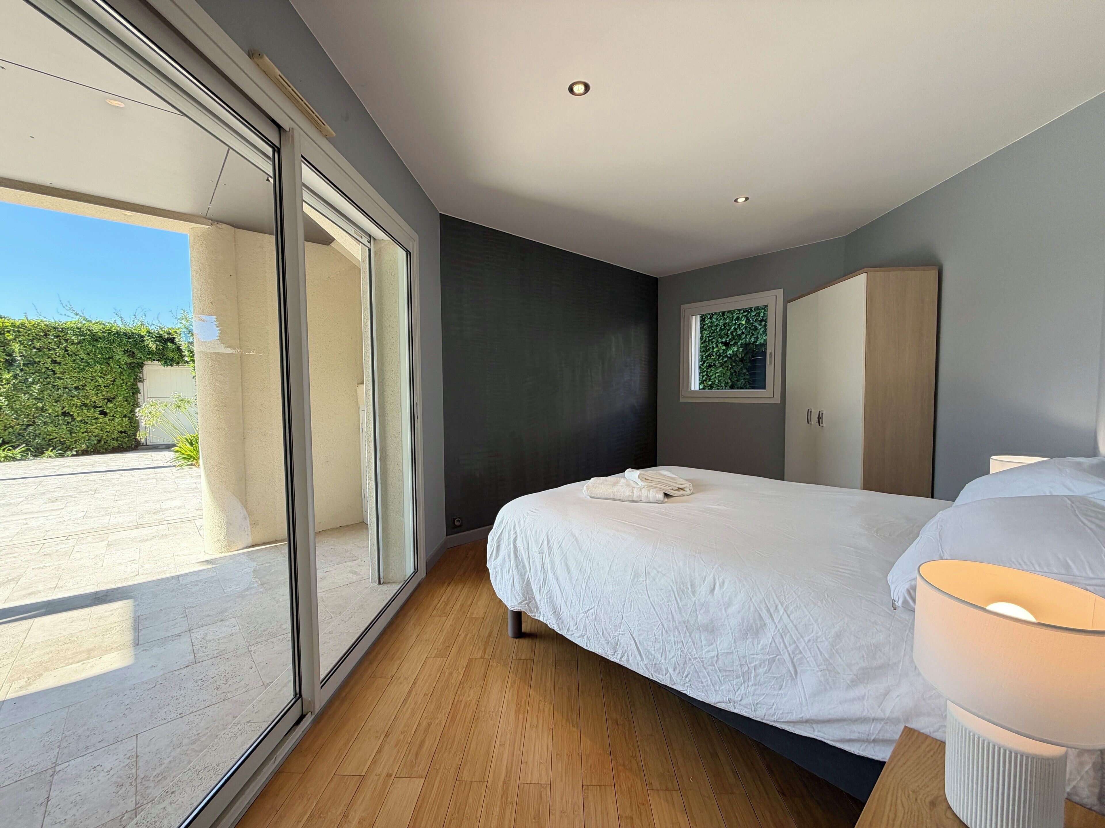 Een moderne slaapkamer met een groot bed, een nachtkastje, een kledingkast en een raam met uitzicht op groen.