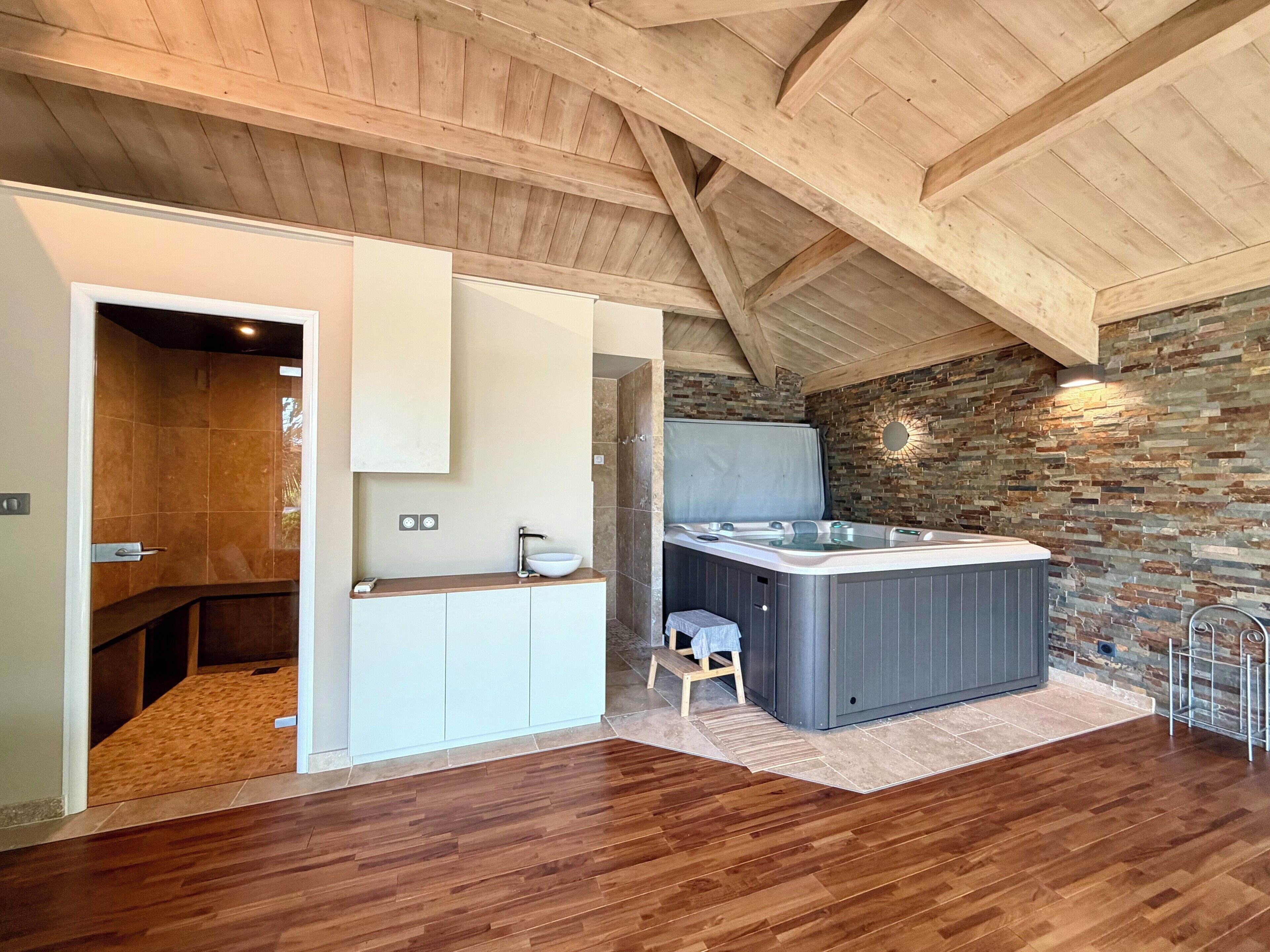 Een moderne badkamer met een houten plafond, een stenen muur, een whirlpool en een houten vloer.