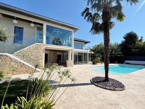 Une maison moderne à deux étages, dotée d’un escalier en pierre, d’une entrée avec porte en verre et d’une piscine.