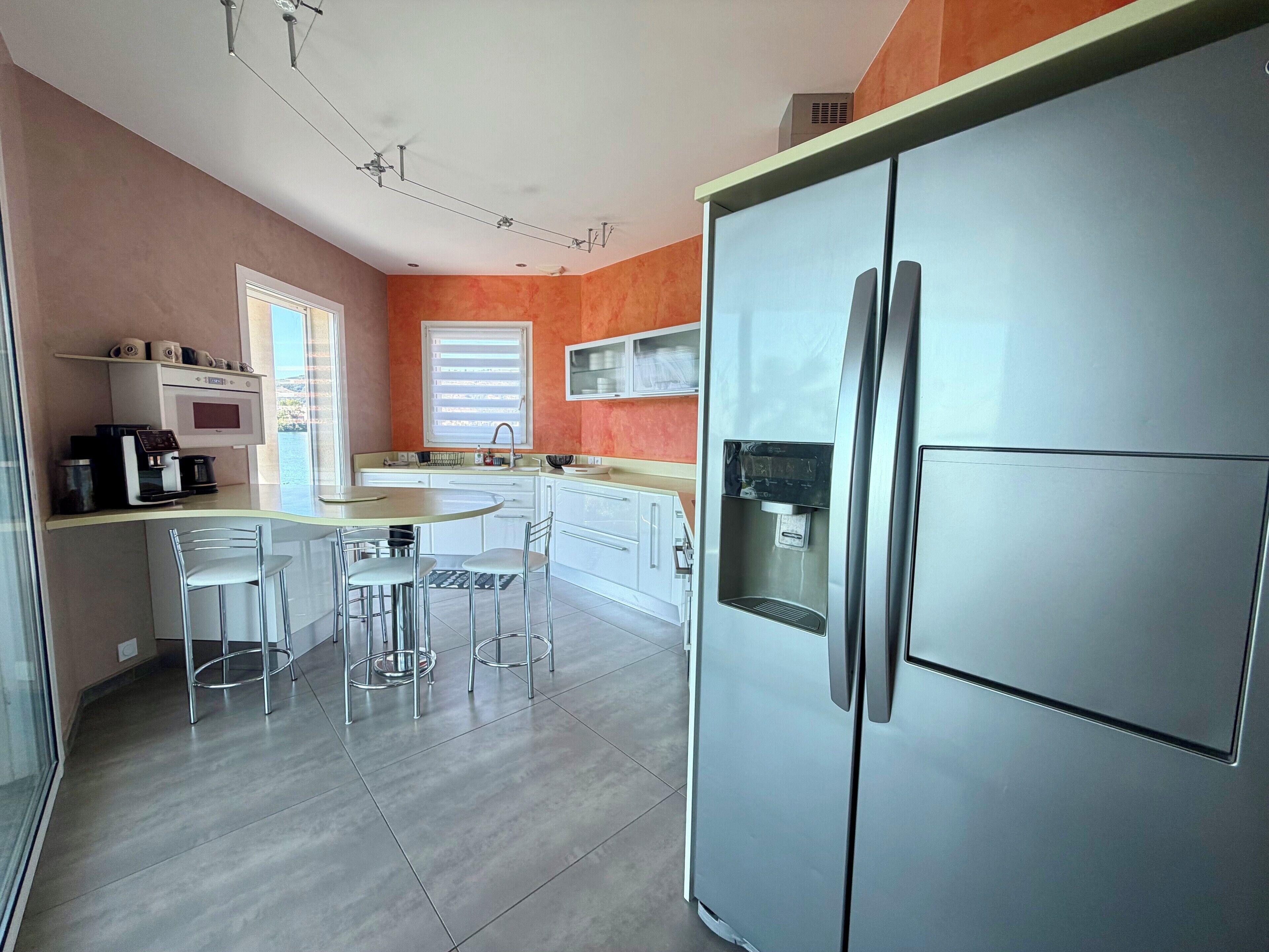 Een moderne keuken met een inbouwkoelkast, een koffieapparaat en een eethoek met stoelen.