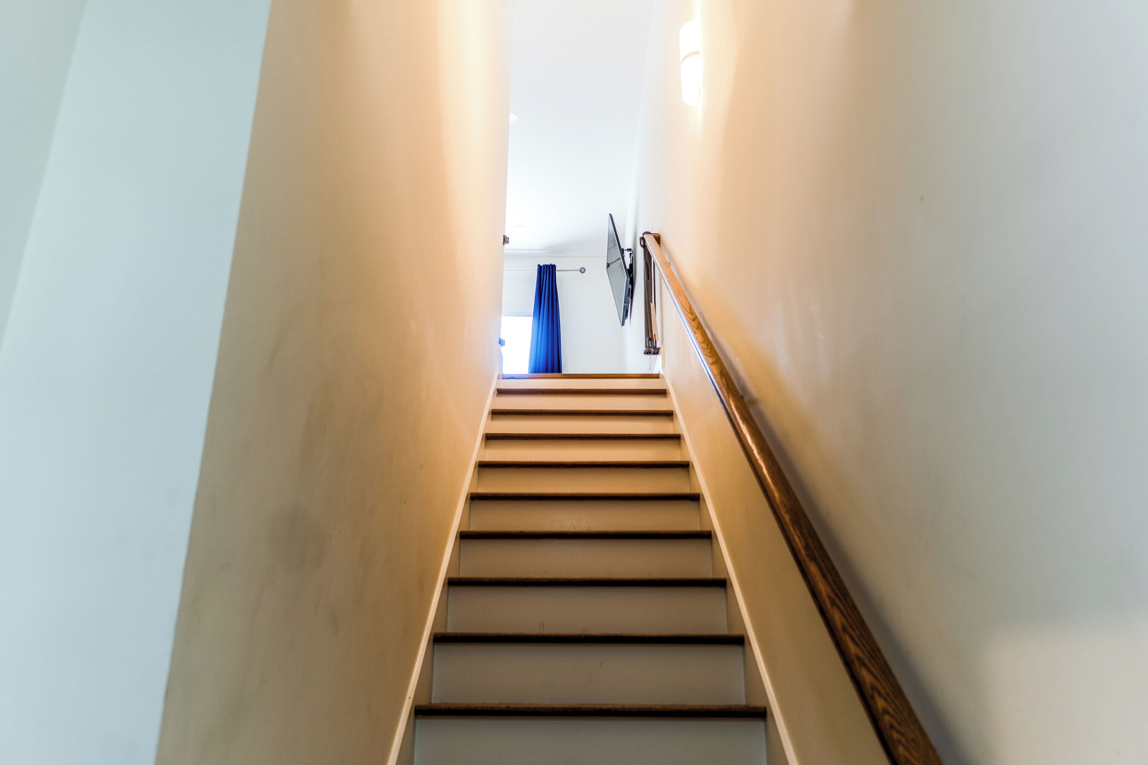 A staircase with a handrail leading to a room with a blue curtain.