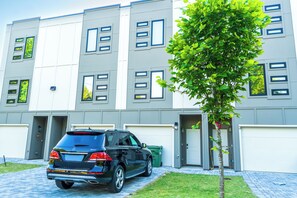 Un edificio moderno con varias puertas de garaje, un coche aparcado y un árbol en primer plano.