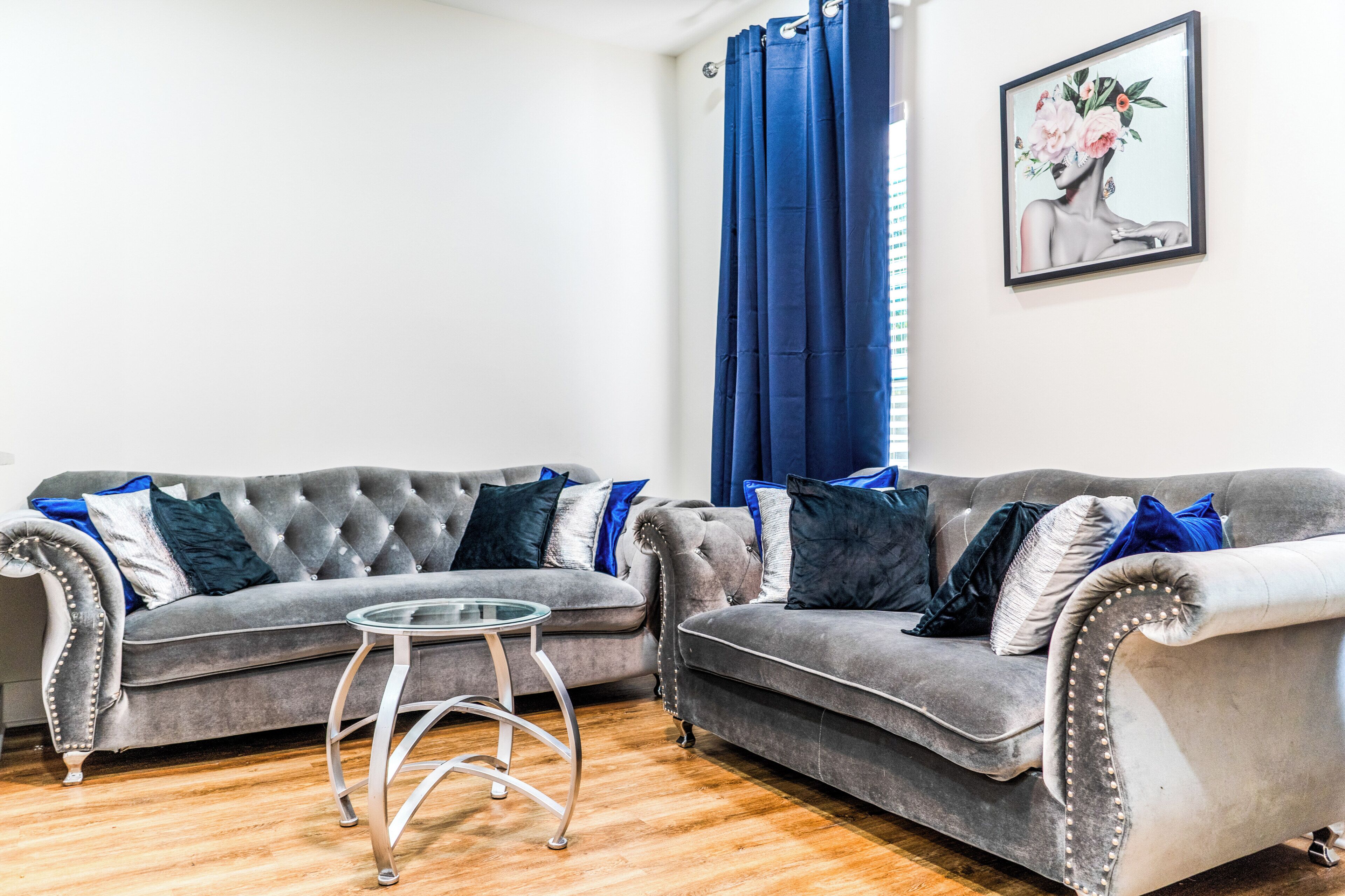 A living room with two grey sofas, a glass coffee table, and a blue curtain.