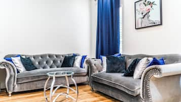 A living room with two grey sofas, a glass coffee table, and a blue curtain.