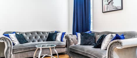 A living room with two grey sofas, a glass coffee table, and a blue curtain.