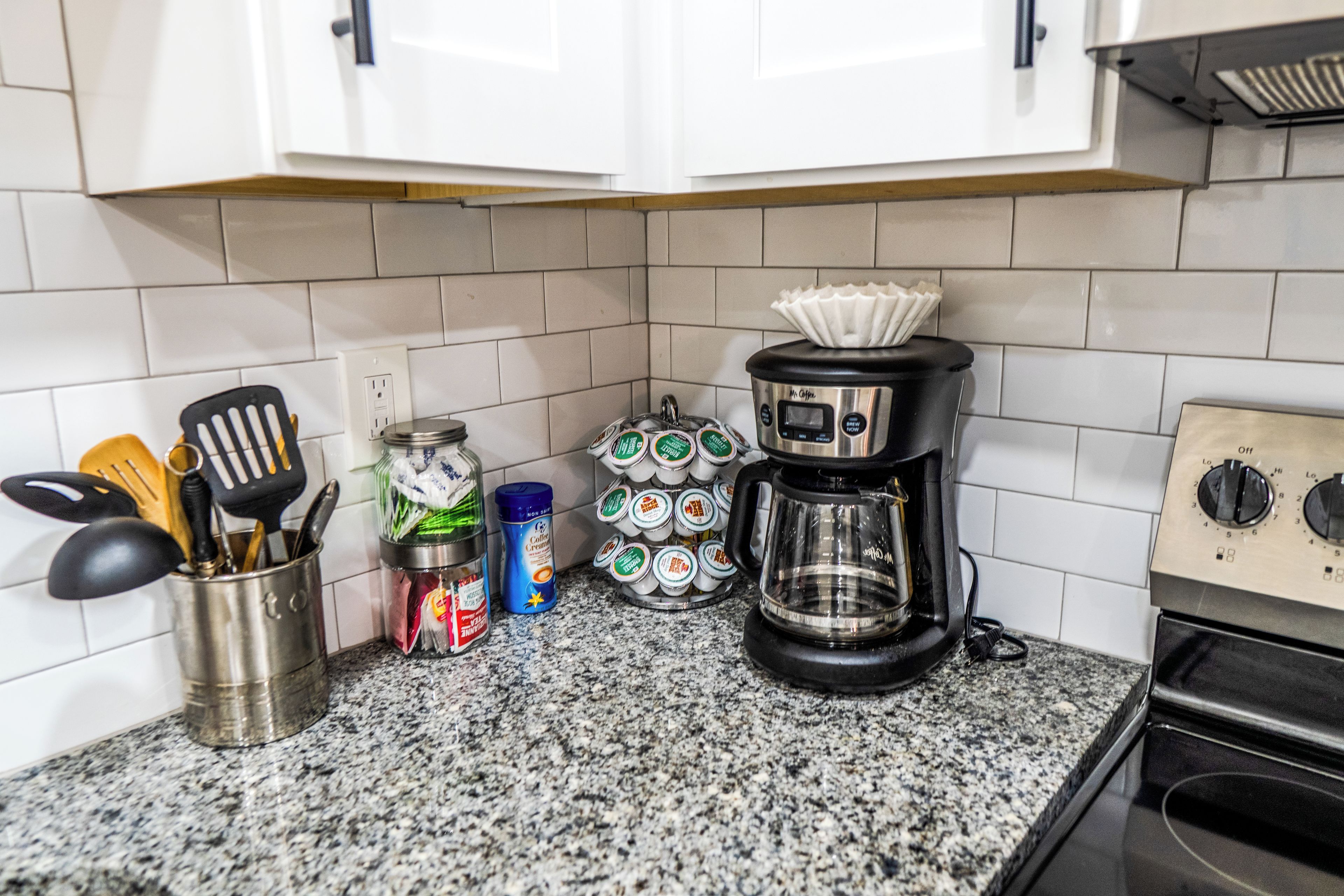 A kitchen with a coffee maker, a jar of coffee creamer, and a container of coffee pods.