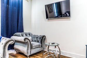 A room with a grey tufted sofa, a small round table, and a flat-screen TV mounted on the wall. - Atlanta Luxe Stay (Atlanta)