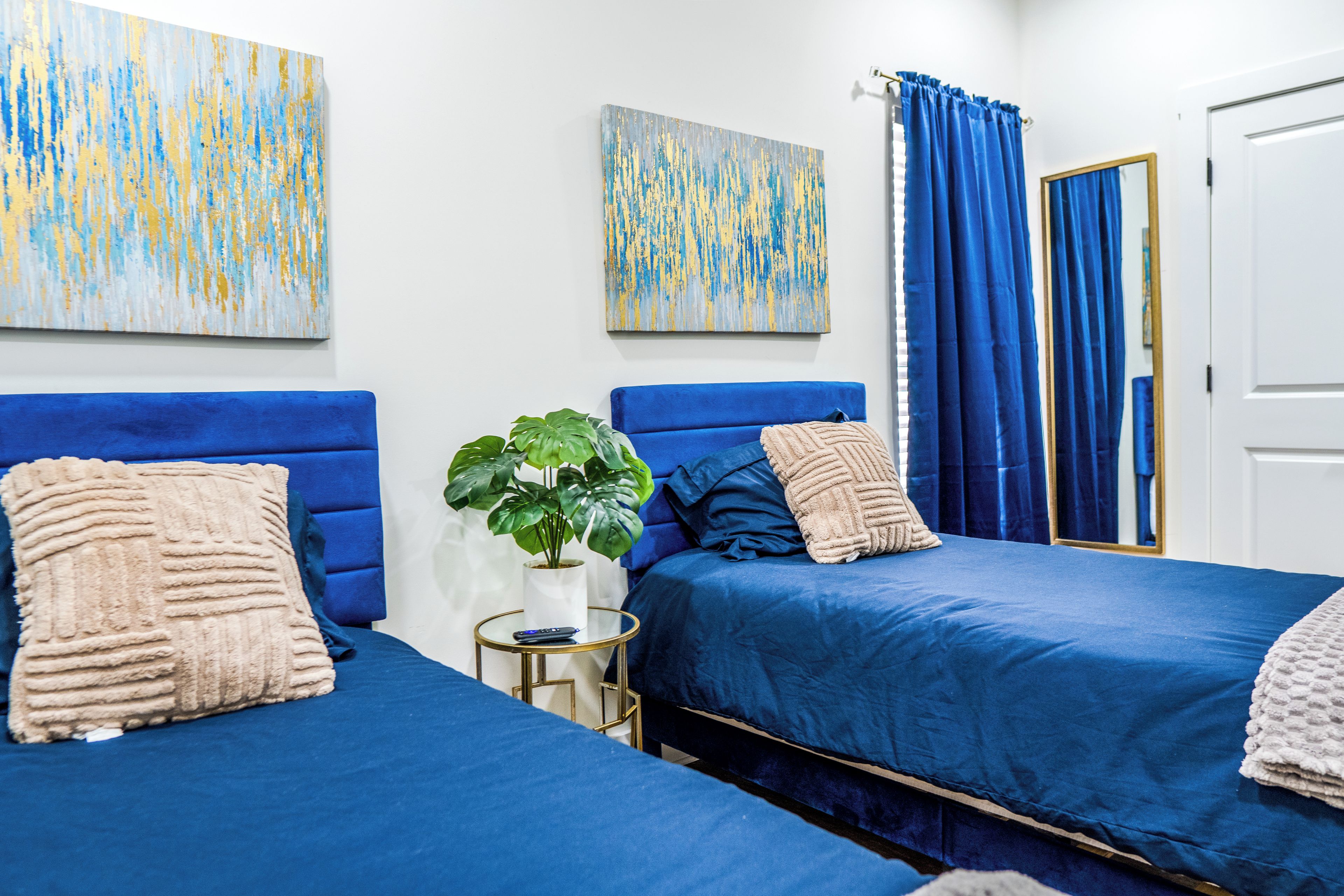 A hotel room with two beds, a potted plant, and artwork on the walls.