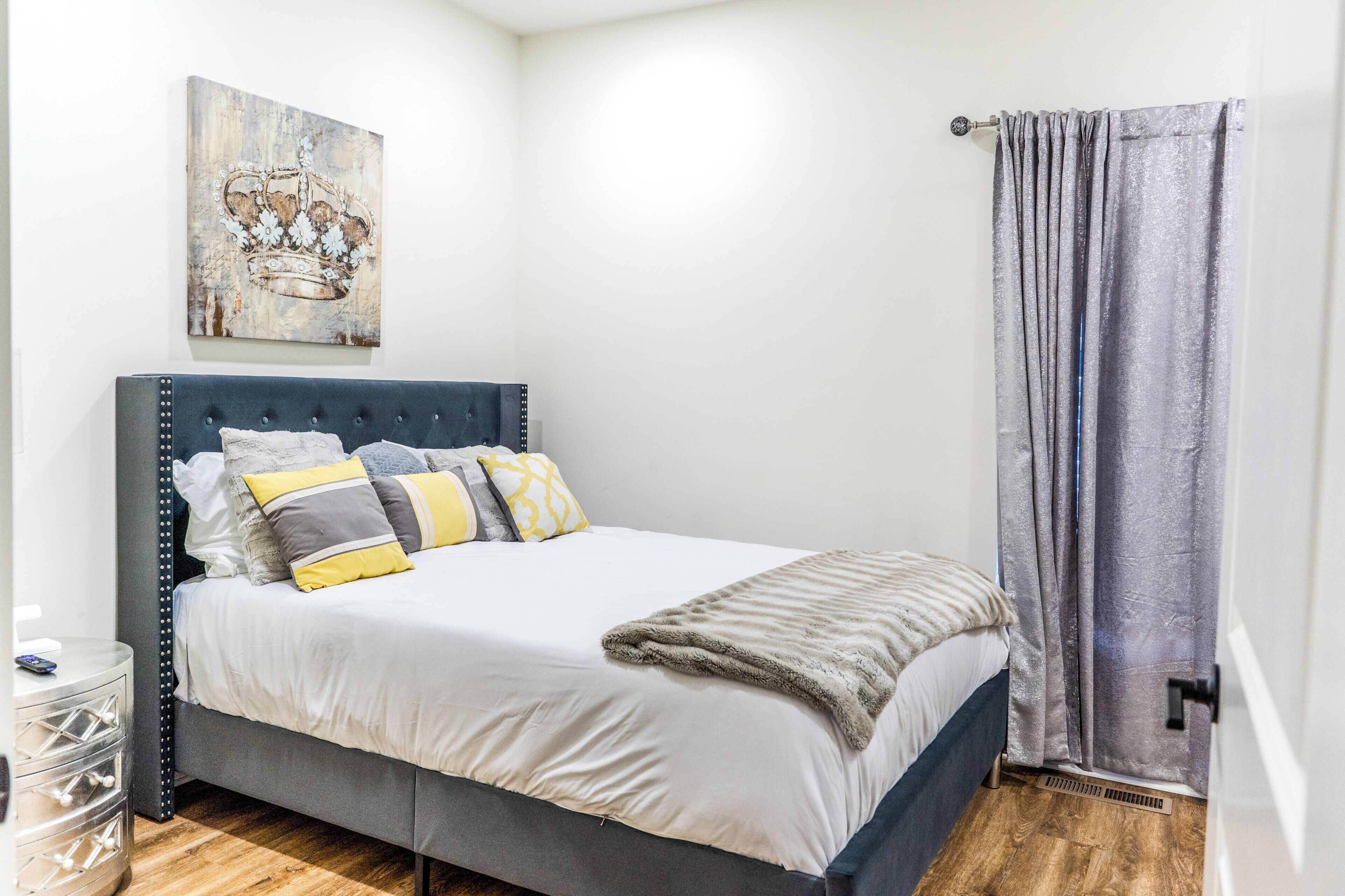 Una cama bien hecha con cabecera gris, ropa de cama blanca y varias almohadas en tonos amarillo y gris.