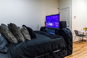 Un dormitorio con cama, televisor, silla y una mesita.