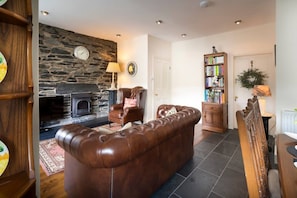 A living room with a stone wall, fireplace, leather sofa, armchair, bookshelf, and a door. - Brantside, Central Ambleside, Panoramic Views (Ambleside)