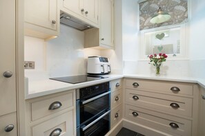 A compact kitchen with a built-in oven, a coffee maker, and a window with a floral curtain. - Brantside, Central Ambleside, Panoramic Views (Ambleside)