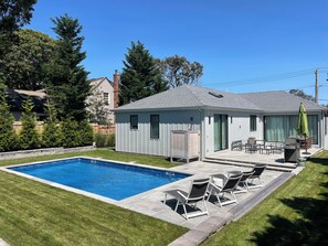 A residential backyard with a swimming pool, patio furniture, and a covered outdoor seating area. - Spacious 4-bedroom house in tranquil Hampton Bays with pool.Close to beach (Hampton Bays)