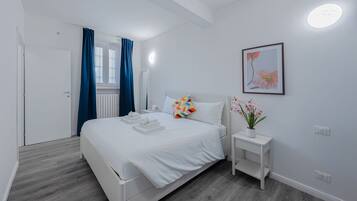A hotel room with a bed, a bedside table with a vase of flowers, a framed picture on the wall, and a door with curtains.