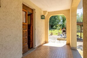 A corridor with a wooden door, a tiled floor, and an archway leading to an outdoor area with a barbecue setup. - La Pineta Holiday Homes - Alfa Apartment (Vallefoglia)