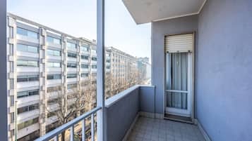 Un balcon donnant sur un immeuble à plusieurs étages, un sol carrelé et une fenêtre avec un store.