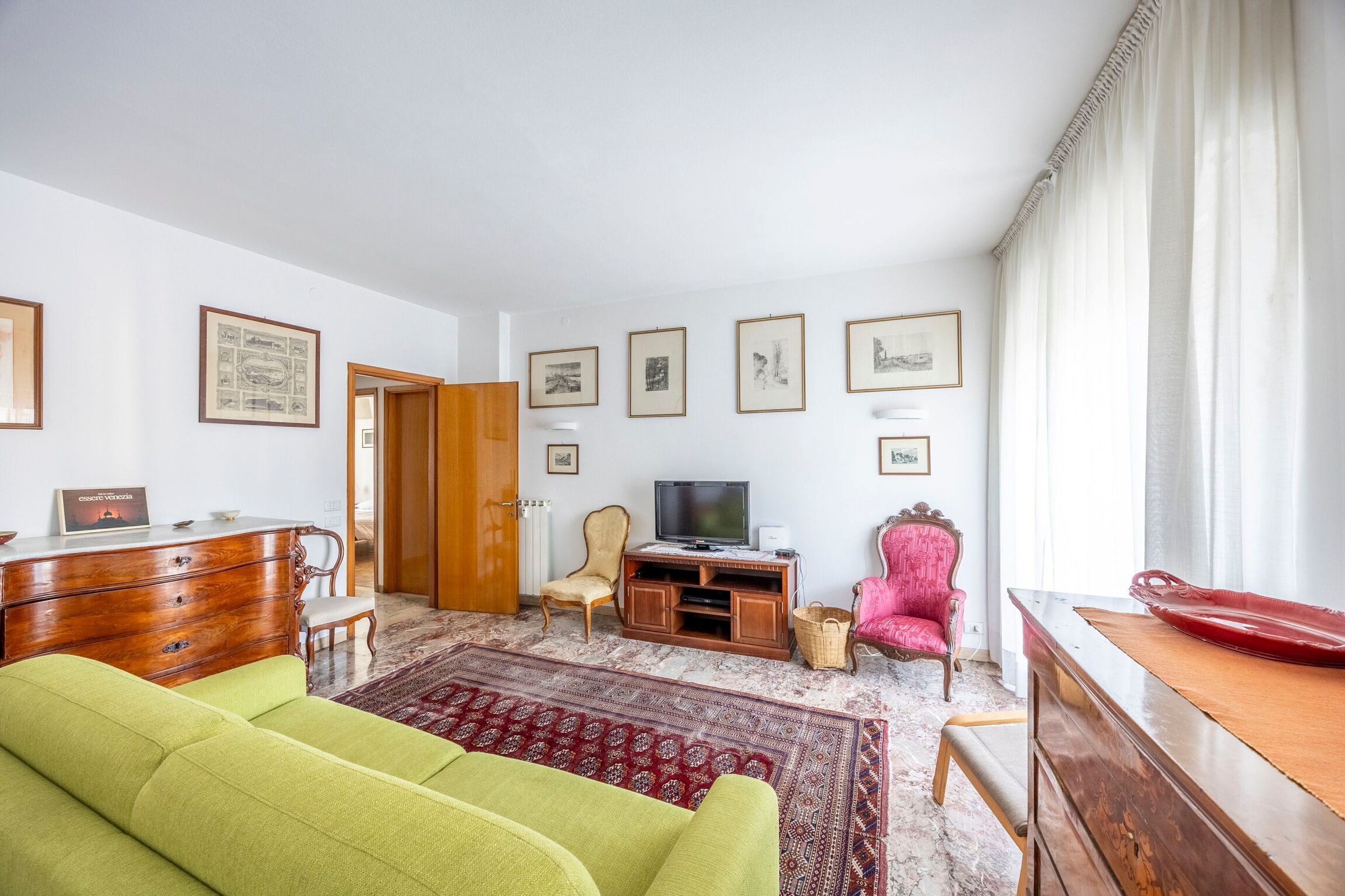 Un salon avec un canapé vert, des meubles en bois, un téléviseur et des tableaux encadrés accrochés au mur.