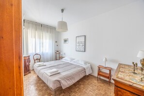 Un dormitori amb un llit, una làmpada penjant, una taula petita i un quadre penjat a la paret.