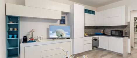 Cocina moderna con muebles blancos, horno empotrado, microondas y un televisor que muestra un oso polar.