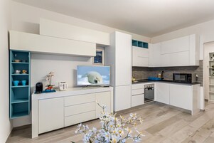 Cocina moderna con muebles blancos, horno empotrado, microondas y un televisor que muestra un oso polar.