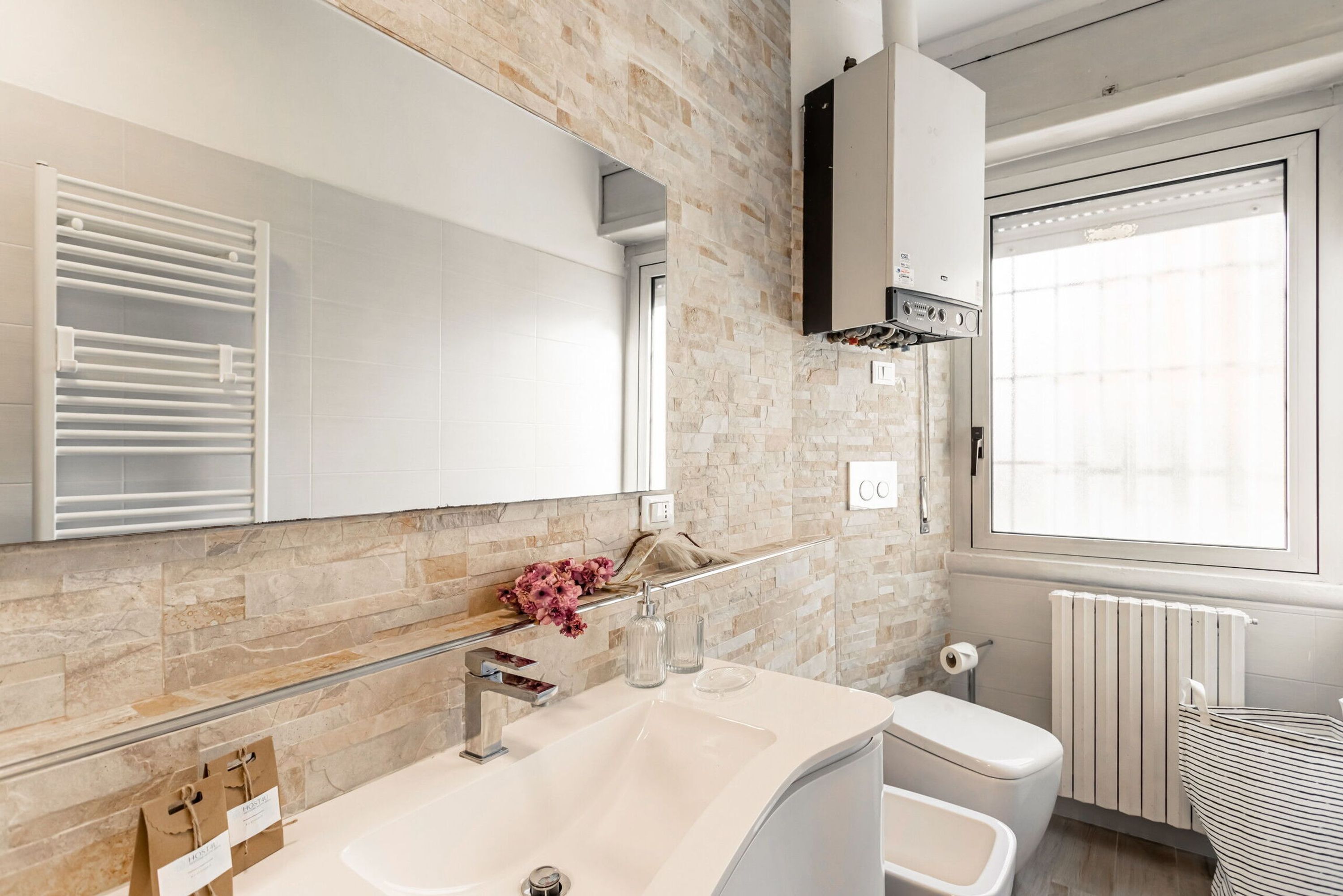 Un bagno moderno con una parete in pietra, un ampio specchio, un lavandino bianco e un water.
